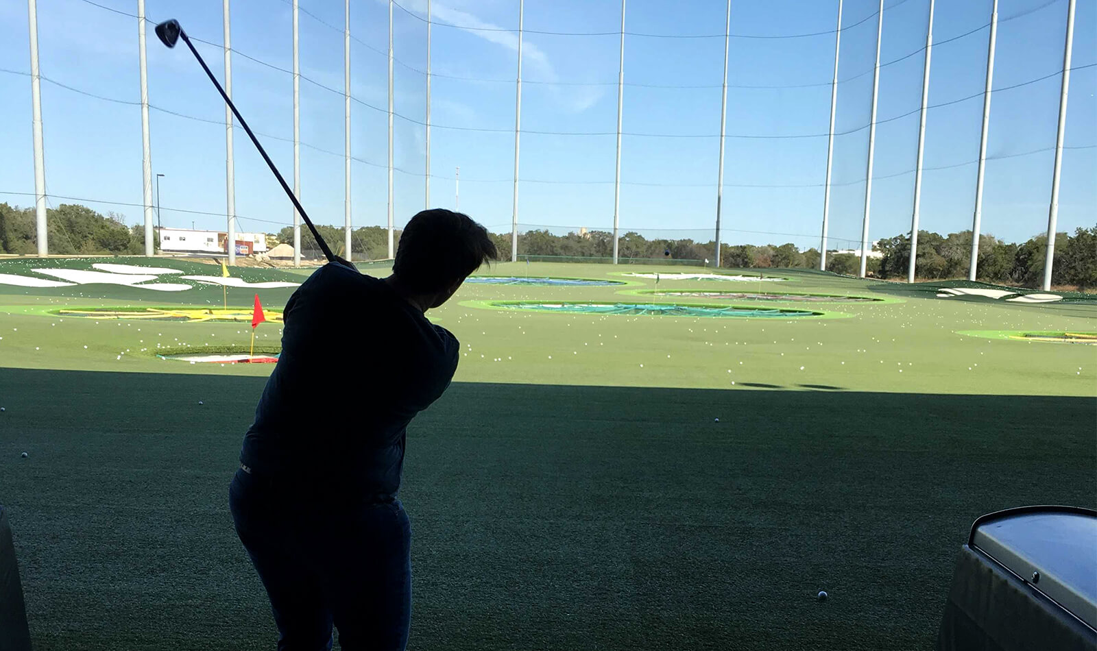 Back view of Grace swinging a golf club at Top Golf.