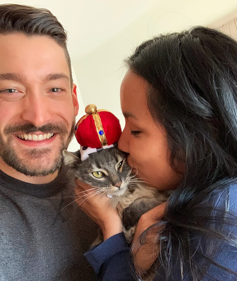 Julia kissing her cat with her boyfriend smiling off to the side.